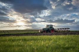 Traktor auf einem Acker, umgeben von Grünland